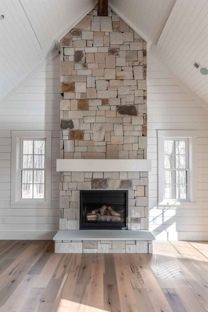 Set against the backdrop of a pristine white nickel pleated wall, the stone farmhouse fireplace makes a subtle but undeniably striking statement in the living room.