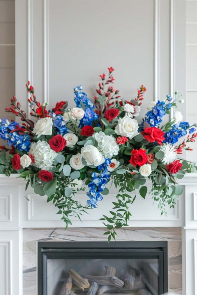 A lively flower arrangement with red, white and blue flowers, including roses and dolphinia, is elegant on a white chimney over a fireplace.
