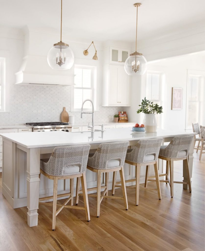 Coastal kitchen with upholstered rattan stools and gold globe pendants