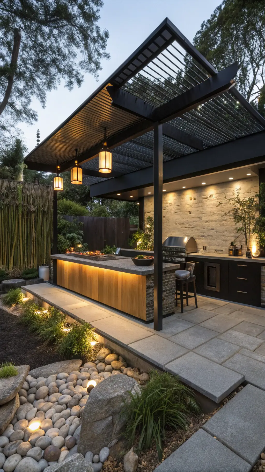 contemporary Asian-fusion outdoor kitchen at twilight with black aluminum pergola, floating concrete counters, built-in teppanyaki grill, paper lantern lighting, and zen rock garden backdrop