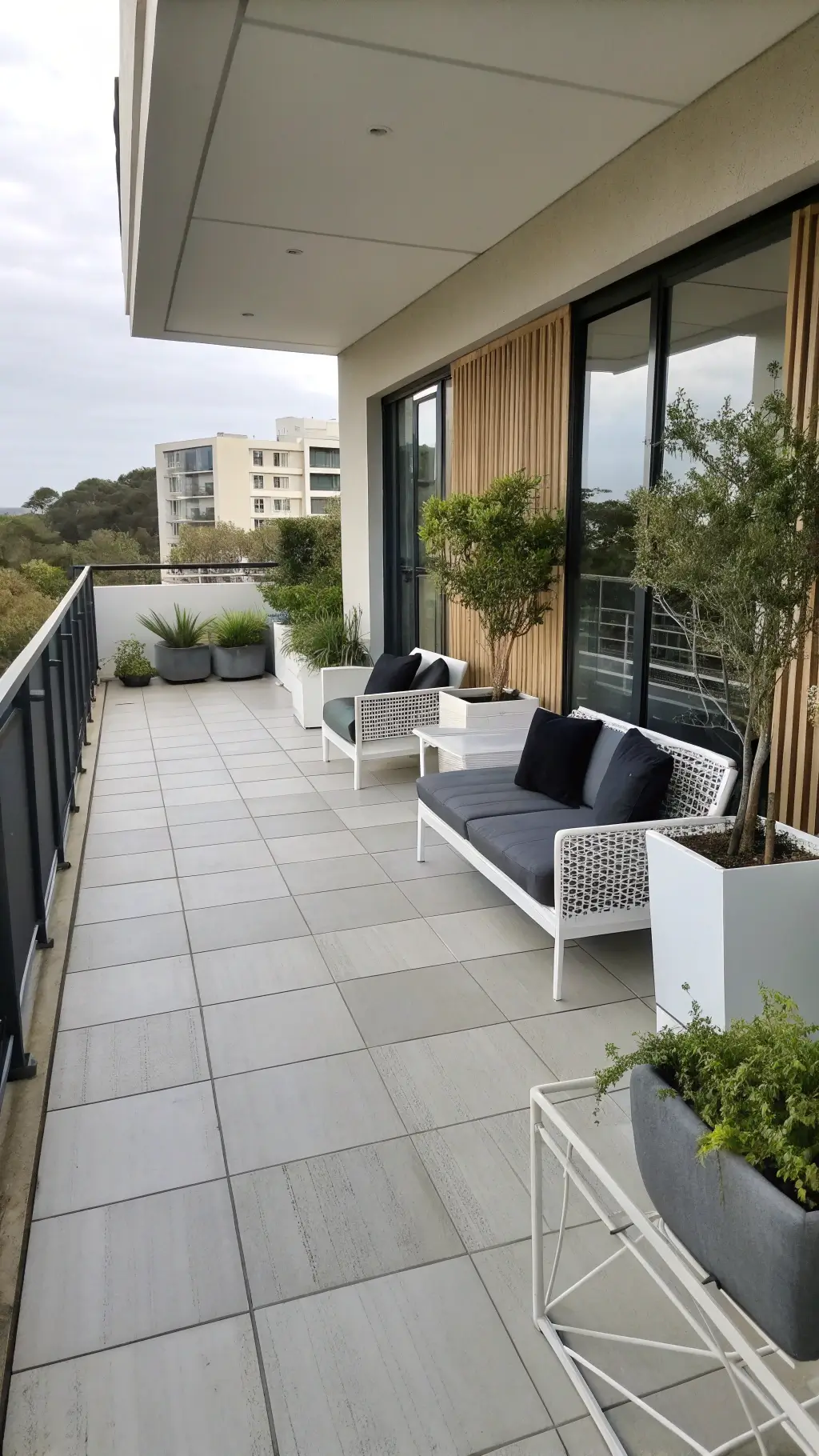 Minimalist balcony design with light grey geometric floor, white metal furniture with charcoal cushions, black planters with bamboo screens, at midday.