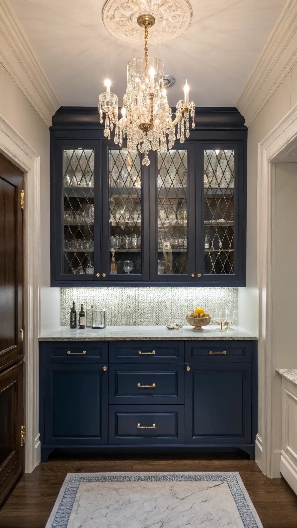 Luxe Butler's Pantry featuring navy blue inset cabinets, crystal chandelier, glass-front upper cabinets showcasing fine china, and polished nickel accessories, shot in mixed lighting for atmospheric depth.