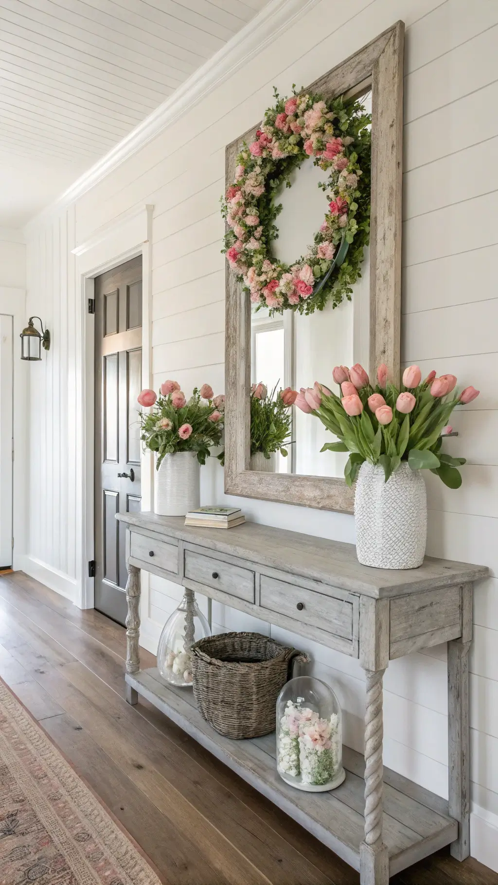 Bright entryway with white shiplap walls, oak flooring, and a vintage mirror reflecting handmade spring wreath; gray console table with mercury glass vases filled with tulips.