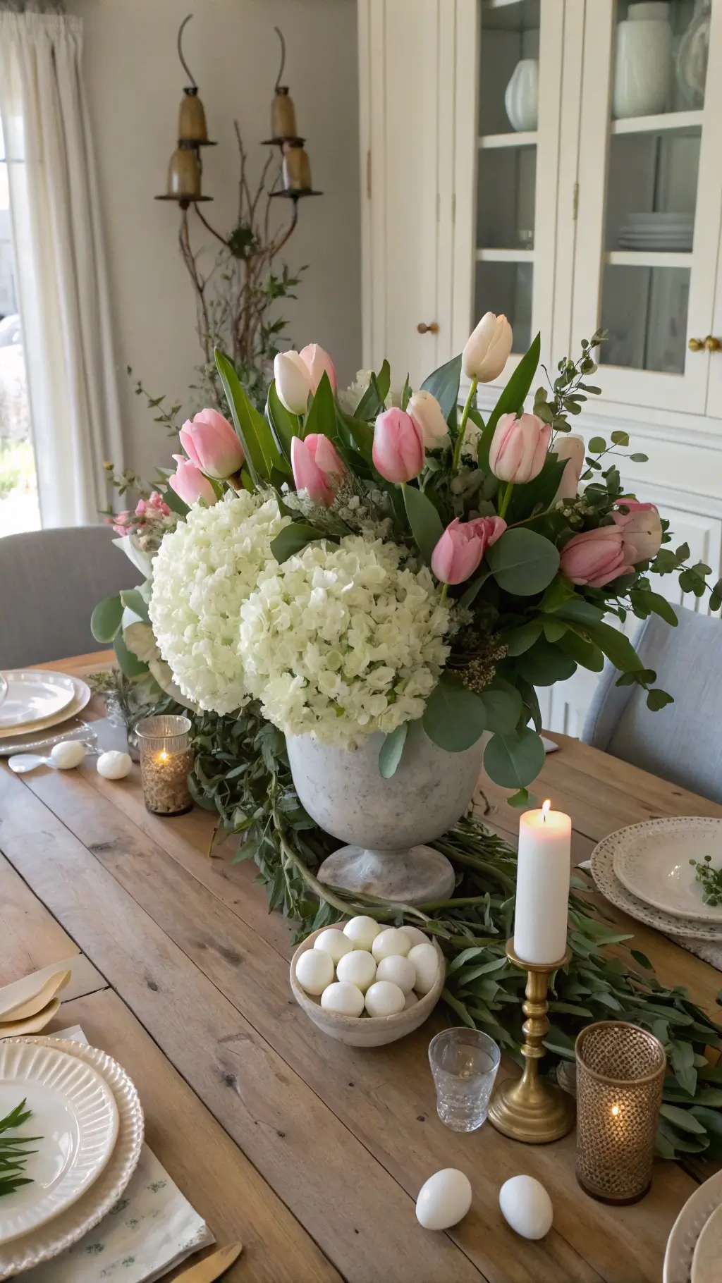 Farmhouse table with white hydrangeas, pink tulips, eucalyptus in ceramic vase, brass eggs, and crystal candlesticks