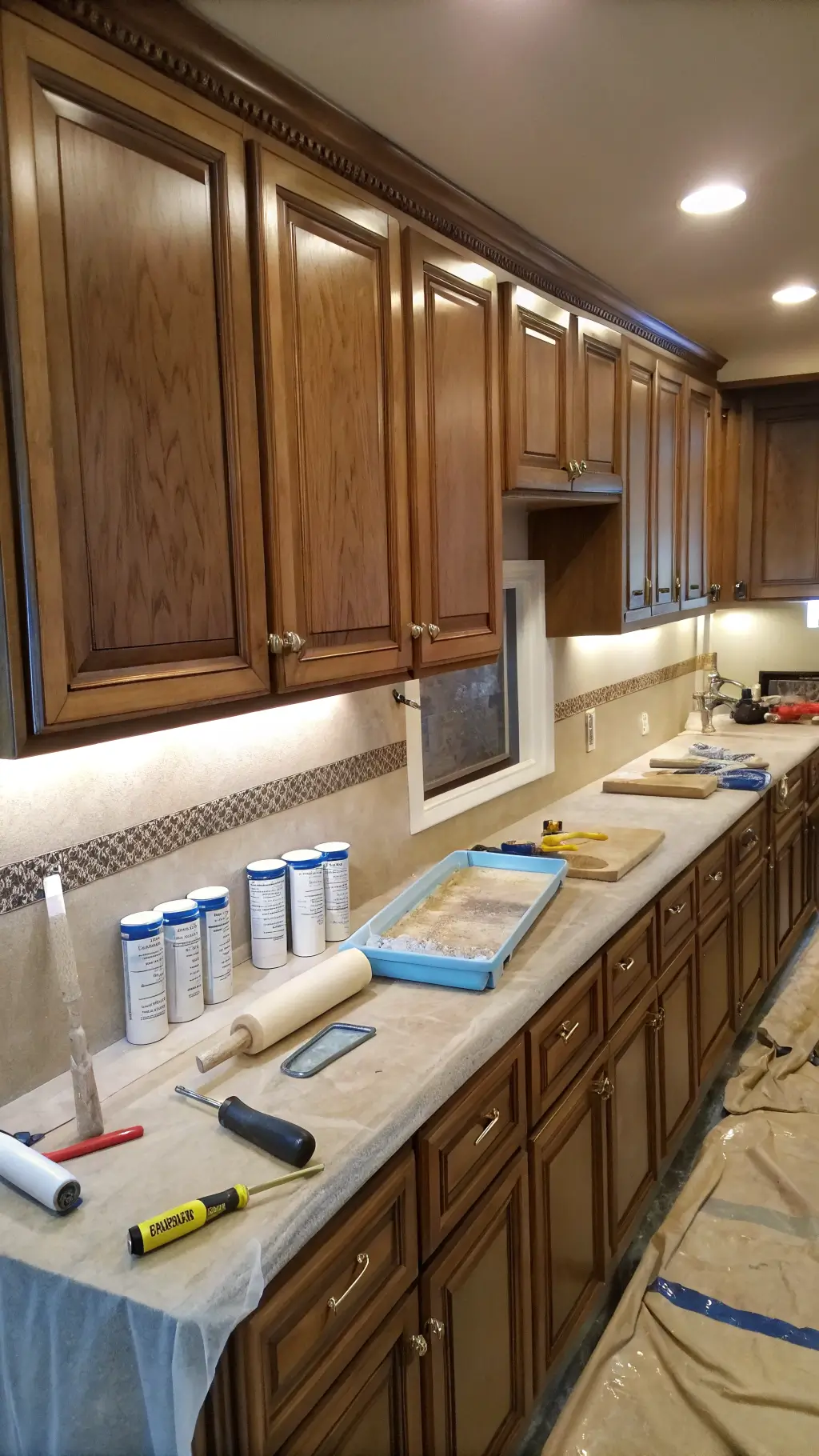 Close-up of kitchen cabinet painting in progress with tools on kraft paper, showing sanded and primed doors under workshop lighting.