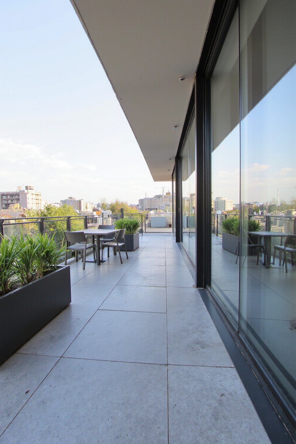 Balcony flooring ideas - Minimalist Sophistication: Grey Stone Flooring with Modern Planters - Use polished grey stone for a sleek balcony floor...